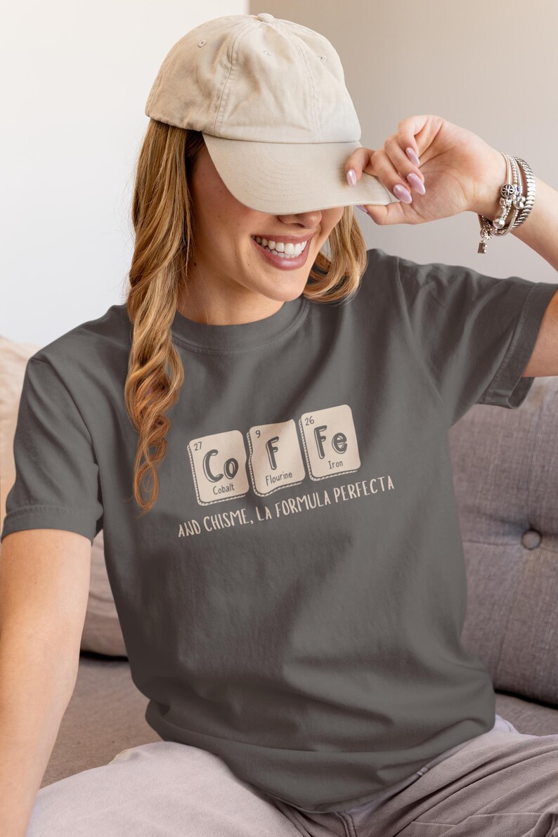 Peut inclure: T-shirt gris fonc&eacute; avec le mot "COFFEE" &eacute;pel&eacute; avec des &eacute;l&eacute;ments du tableau p&eacute;riodique. Le t-shirt porte &eacute;galement l'inscription "AND CHISME, LA FORMULA PERFECTA" en dessous.