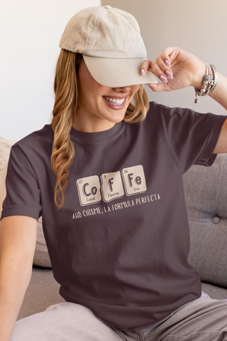 Peut inclure: T-shirt violet fonc&eacute; avec le mot "COFFEE" &eacute;pel&eacute; avec des &eacute;l&eacute;ments du tableau p&eacute;riodique. Le t-shirt porte &eacute;galement l'inscription "AND CHISME, LA FORMULA PERFECTA" en dessous.