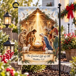 May include: A rectangular garden flag featuring a nativity scene with a bright star above a wooden stable, Mary, Joseph, the infant, and three figures. Below, a scroll displays the text The Greatest Gift of All. Matthew 1:21.