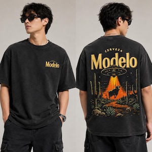 May include: Black t-shirt with the word "Modelo" in gold on the front. The back features a desert scene with a bull, cacti, and a UFO with the words "Cerveza Modelo" in gold.