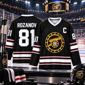 May include: A black hockey jersey featuring a white V-neck, white and red stripes on the sleeves and hem, and a yellow cannon logo with an R on the chest. The back displays the name ROZANOV and the number 81 in white block lettering.