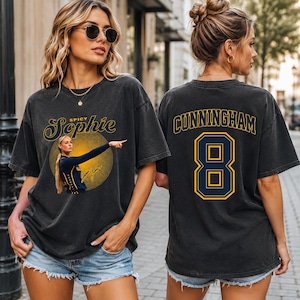 May include: A charcoal gray short-sleeve t-shirt featuring a front graphic of a basketball player with the text Spicy Sophie and a back graphic with the name CUNNINGHAM and the number 8 in yellow and navy blue lettering on the back of the shirt.