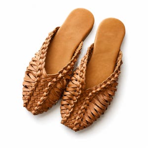 Puede incluir: Un par de zapatos sin cordones de cuero marrón claro con tejido. Los zapatos tienen un diseño trenzado alrededor de los bordes y una plantilla de cuero macizo. Estos zapatos están diseñados para la comodidad y el estilo.