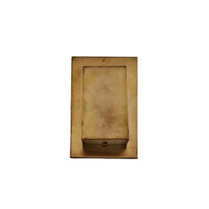 May include: A rectangular brass box with a smooth, metallic finish and a slightly weathered patina. The object features a centered, raised rectangular lid section with a small, circular knob at the bottom edge, set against a flat base plate.