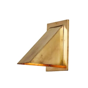 May include: A wall-mounted light fixture featuring a triangular, wedge-shaped brass shade attached to a rectangular backplate. The metallic surface has a warm, brushed gold finish, and the open bottom edge emits a soft, warm glow of light.