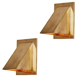 May include: A pair of wall-mounted light fixtures crafted from brass with a rectangular backplate and a triangular, angled shade that directs light downward. The metal surface features a warm, metallic finish with subtle variations in tone.