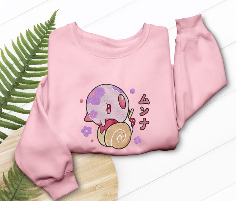 Peut inclure: Un sweat-shirt &agrave; manches longues rose clair orn&eacute; d'un motif repr&eacute;sentant une cr&eacute;ature ronde &agrave; taches violettes pos&eacute;e sur une p&acirc;tisserie beige en forme de spirale avec une fraise. Le dessin inclut des fleurs violettes et le texte japonais ムンナ.