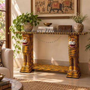 May include: A rectangular console table featuring two hand-carved tiger figures as legs, painted in vibrant yellow with black stripes, white accents on the faces, and red mouths. The table has a flat top surface and a lower shelf, both with tiger patterns.