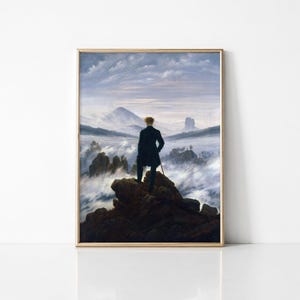 Könnte beinhalten: Ein gerahmter Druck eines Gemäldes, das eine Person in einem dunklen Mantel auf einer felsigen Klippe zeigt, die über eine weite Landschaft aus dichtem weißem Nebel, zerklüfteten Berggipfeln und einem blassblauen, bewölkten Himmel blickt.
