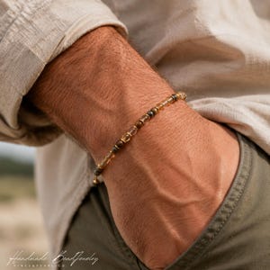 May include: A beaded bracelet featuring a repeating pattern of small, translucent amber-colored beads and dark, metallic-toned spherical beads, strung together on a thin cord to form a circular wrist accessory.
