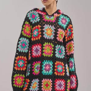 May include: Black crochet hoodie and matching pants set. The hoodie and pants are made of colorful granny squares in shades of pink, orange, green, and purple. The hoodie has a hood and long sleeves.