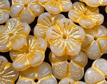 May include: A collection of white flower-shaped beads with gold accents. The beads have a slightly textured surface and a hole in the center.