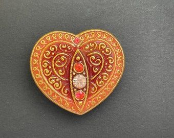 May include: A heart-shaped brooch with a red and gold filigree design and a cluster of red and clear rhinestones in the center.