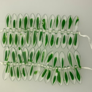 May include: A strand of clear glass beads with green leaf designs. The beads are strung on white thread.