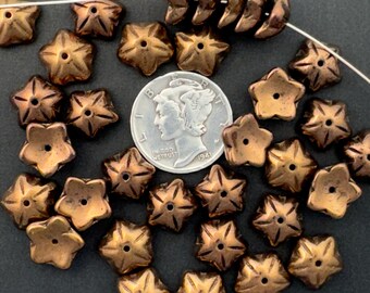 May include: A group of 25 copper-colored glass star-shaped beads with a hole in the center. The beads are approximately the size of a US dime.
