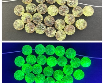 May include: A selection of round, textured beads in shades of yellow and brown, strung on a white thread. The beads have a distinctive, bumpy surface. The bottom image shows the same beads glowing bright green under a black light.
