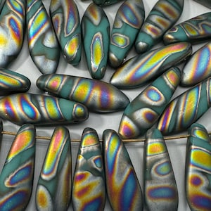 Peut inclure: Un ensemble de perles en verre irisées dans des tons de bleu sarcelle, vert et argent. Les perles sont allongées et présentent un motif marbré.