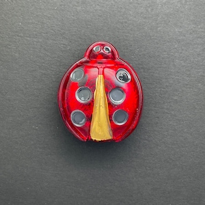 May include: A red glass ladybug with black spots and a gold wing design.