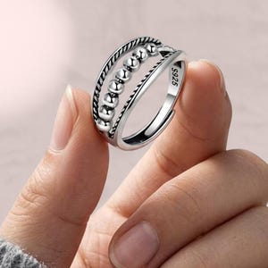 May include: A silver ring featuring a band with a twisted rope texture and a central row of small, movable spherical beads. The interior of the band is clearly stamped with the hallmark S925, indicating the sterling silver composition of the piece.