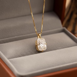 Peut inclure: Un collier en or avec un grand pendentif rectangulaire en pierre précieuse transparente. Le pendentif est serti dans un cadre en or et suspendu à une fine chaîne en or. Le collier est présenté dans un écrin gris avec un extérieur marron.