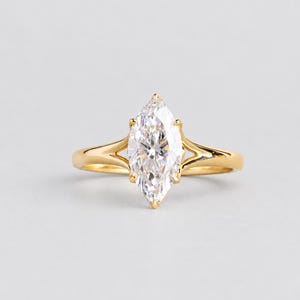 Könnte beinhalten: Ein Goldring mit einem einzelnen, im Marquise-Schliff facettierten, klaren Edelstein, der von sechs Krappen gehalten wird. Die Ringschiene hat ein gespaltenes Design, bei dem sich die Metallarme zum Mittelstein hin teilen und glänzen.