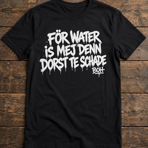 Könnte beinhalten: Schwarzes T-Shirt mit weißem Text "FÖR WATER is MEJ DENN DORST TE SCHADE". Der Text hat einen tropfenden Farbeffekt. Das Shirt wird auf einer Holzoberfläche präsentiert.