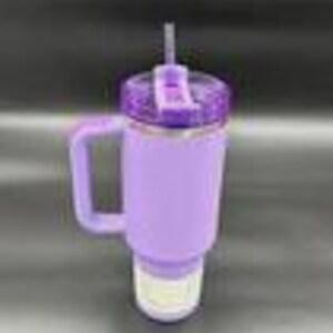 May include: A purple insulated tumbler with a handle and a straw. The tumbler has a textured, non-slip sleeve and a glittery lid. The tumbler is designed to keep drinks cold for hours.