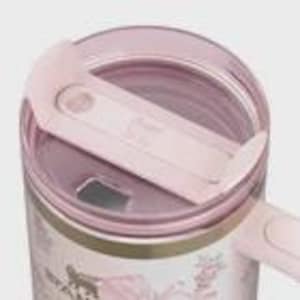 Puede incluir: Primer plano de un termo de viaje rosa y blanco con tapa transparente y cierre deslizante. El termo presenta un dise&ntilde;o floral con detalles dorados. El termo es de acero inoxidable.