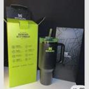 May include: A black Stanley tumbler with a handle and straw, shown with its packaging. The box is lime green with white text and icons. A black lid and a black box with a logo are also visible.