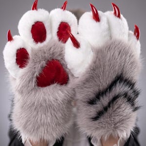 May include: Furry gray and white paw gloves with red paw pads and long, red claws. The gloves have a realistic design, with a soft, plush texture. The gloves are a costume accessory.