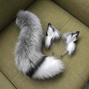 May include: A set of faux fur animal ears on a thin headband and a matching long, bushy tail. The fur is a blend of grey, white, and black tones, featuring a thick, soft texture with a dark band near the tip of the tail and white inner ears.