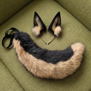 Op de afbeelding: Een set van imitatiebont dierenoren op een dunne haarband en een bijpassende lange imitatiebont staart. De oren en staart hebben een patroon van zwart en beige synthetisch bont. De staart is voorzien van een zwarte verstelbare riem met gesp.