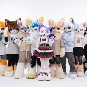 May include: A collection of people in vibrant animal costumes, including foxes, cats, and wolves. The costumes have large heads, fluffy fur, and detailed designs. The group is standing together, posing for a photo against a plain background.