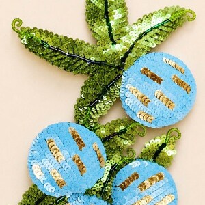 Puede incluir: Parche floral bordado con formas azules con lentejuelas en forma de flor y hojas verdes con lentejuelas. Las formas de flor tienen detalles de lentejuelas doradas. El texto "ONLY PATCH" está en la parte superior.