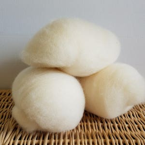 以下が含まれることがあります： 籐の表面に置かれた、白いふわふわした羊毛のボールが3つ