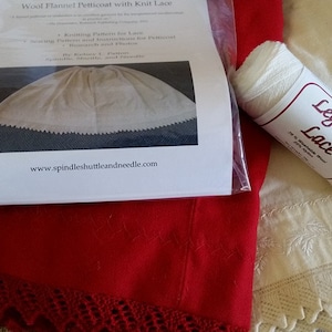 May include: A white spool of thread labeled "Legacy Lace" with a white petticoat and a red flannel petticoat with a crocheted trim. The image also includes a printed pattern for a wool flannel petticoat with knit lace.
