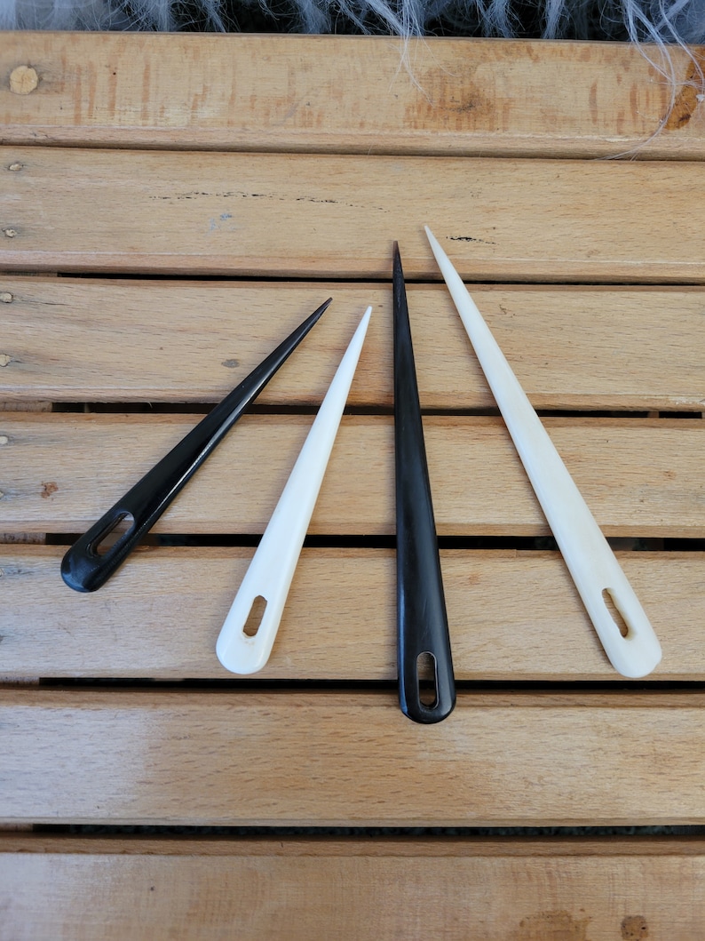 May include: Four knitting needles, two black and two white, arranged in a V shape on a wooden surface.