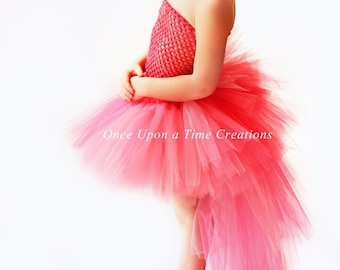 May include: A young girl wearing a pink tulle tutu with a long train. The tutu has a pink crocheted bodice. She is wearing a pink flower headband and has red hair. The text "Once Upon a Time Creations" is visible on the tutu.