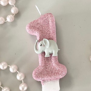 Könnte beinhalten: Rosa glitzernde Zahl eins Geburtstagskerze mit einer weißen Elefantenfigur auf der Vorderseite.