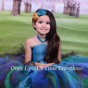 May include: A young girl wearing a blue and green tulle tutu with a blue crocheted halter top and a flower headband. The text "Once Upon A Time Creations" is visible in the image.