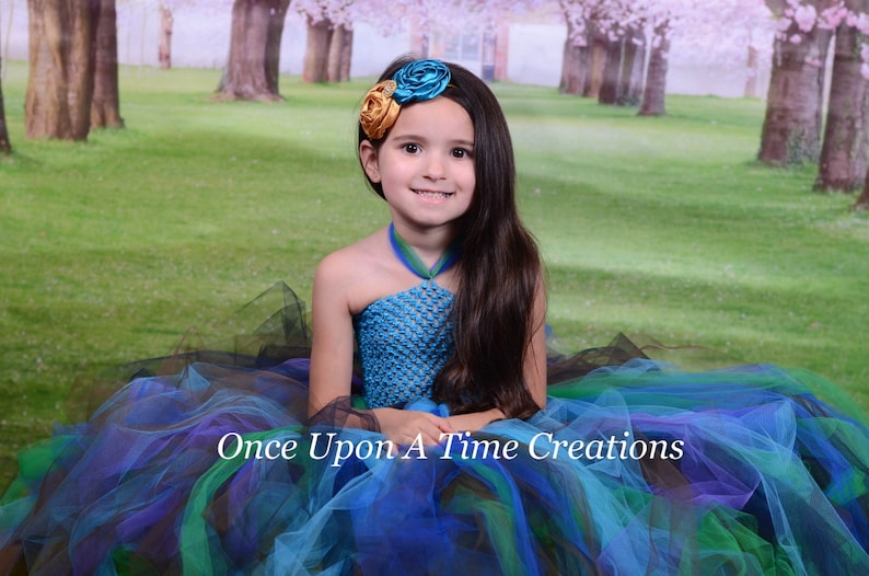 May include: A young girl wearing a blue and green tulle tutu with a blue crocheted halter top and a flower headband. The text "Once Upon A Time Creations" is visible in the image.