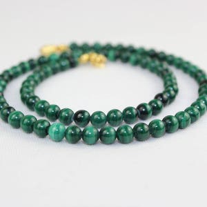 May include: A green malachite bead necklace with a gold clasp. The necklace is made of round beads and is layered twice.