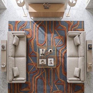 May include: A top-down view of a living room featuring two beige sofas facing each other, separated by a square glass coffee table. A large area rug with a blue and orange geometric pattern lies beneath the furniture. A wooden console table sits at the top.