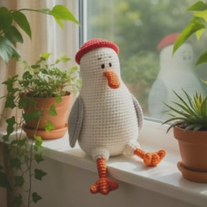 May include: A handmade crochet seagull doll with a red beret, orange beak, and feet. The seagull has gray wings and is sitting on a windowsill. The doll is surrounded by potted plants, creating a cozy, whimsical scene.