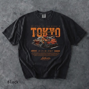 May include: Black t-shirt featuring a graphic of a stylized orange sports car with the word "TOKYO Underground" in orange. The shirt includes Japanese text and the word "Authentic" in a vintage style.