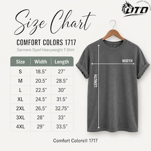 K&ouml;nnte beinhalten: Ein anthrazitfarbenes Comfort Colors 1717 T-Shirt aus schwerem, st&uuml;ckgef&auml;rbtem Stoff auf einem Holzkleiderb&uuml;gel neben einer Gr&ouml;&szlig;entabelle. Die Tabelle f&uuml;hrt die Gr&ouml;&szlig;en S bis 4XL mit den entsprechenden Breiten- und L&auml;ngenma&szlig;en in Zoll auf.