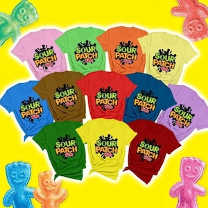 May include: A collection of eleven short-sleeve t-shirts in various solid colors, each featuring the Sour Patch Kids logo printed in black, yellow, and orange on the chest, arranged against a bright yellow background with candy figures.
