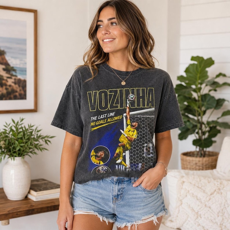 Peut inclure: Un t-shirt gris anthracite &agrave; manches courtes avec une impression graphique d'un gardien de but de football en maillot jaune effectuant un arr&ecirc;t. Le texte indique VOZINHA, THE LAST LINE et NO GOALS ALLOWED. Le t-shirt a un aspect d&eacute;lav&eacute; vintage.