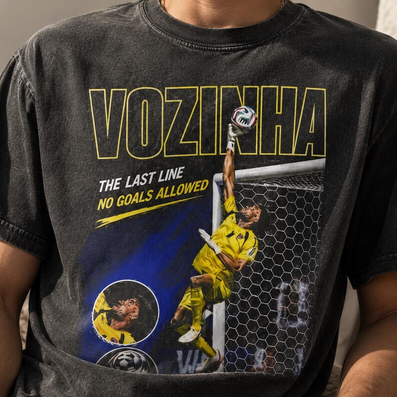 Peut inclure: Un t-shirt noir anthracite avec un graphisme repr&eacute;sentant un gardien de but en uniforme jaune sautant pour attraper un ballon. Le texte indique VOZINHA, THE LAST LINE et NO GOALS ALLOWED. Le design inclut un encart circulaire du visage.