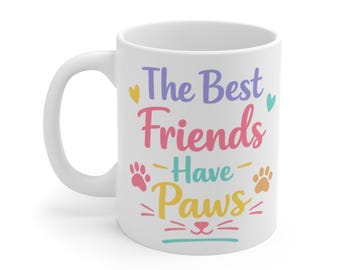 May include: A white ceramic mug featuring the colorful text The Best Friends Have Paws. The design includes a small yellow heart, a teal heart, two pink paw prints, one orange paw print, and a stylized cat nose and whiskers in pink and teal.